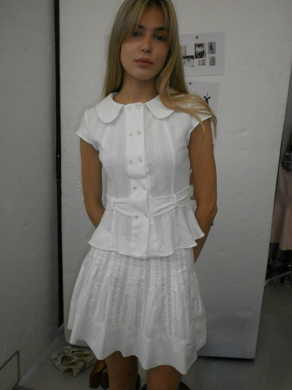 Model wearing the Virginia Blouse Pointelle in white, cute Double breasted shell buttons and cute peter pan collar design cap short sleeve blouse in a indoor setting– independent designer womenswear by A Room London